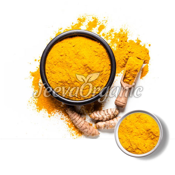 A black bowl filled with vibrant yellow turmeric powder, surrounded by turmeric roots and a small spoonful of powder.