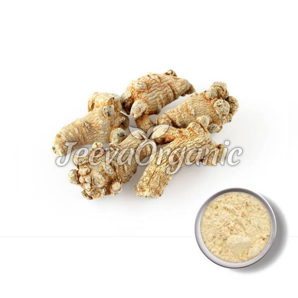 Four dried, irregularly shaped ginger roots with a small bowl of ginger powder in the corner, showcasing their culinary uses.