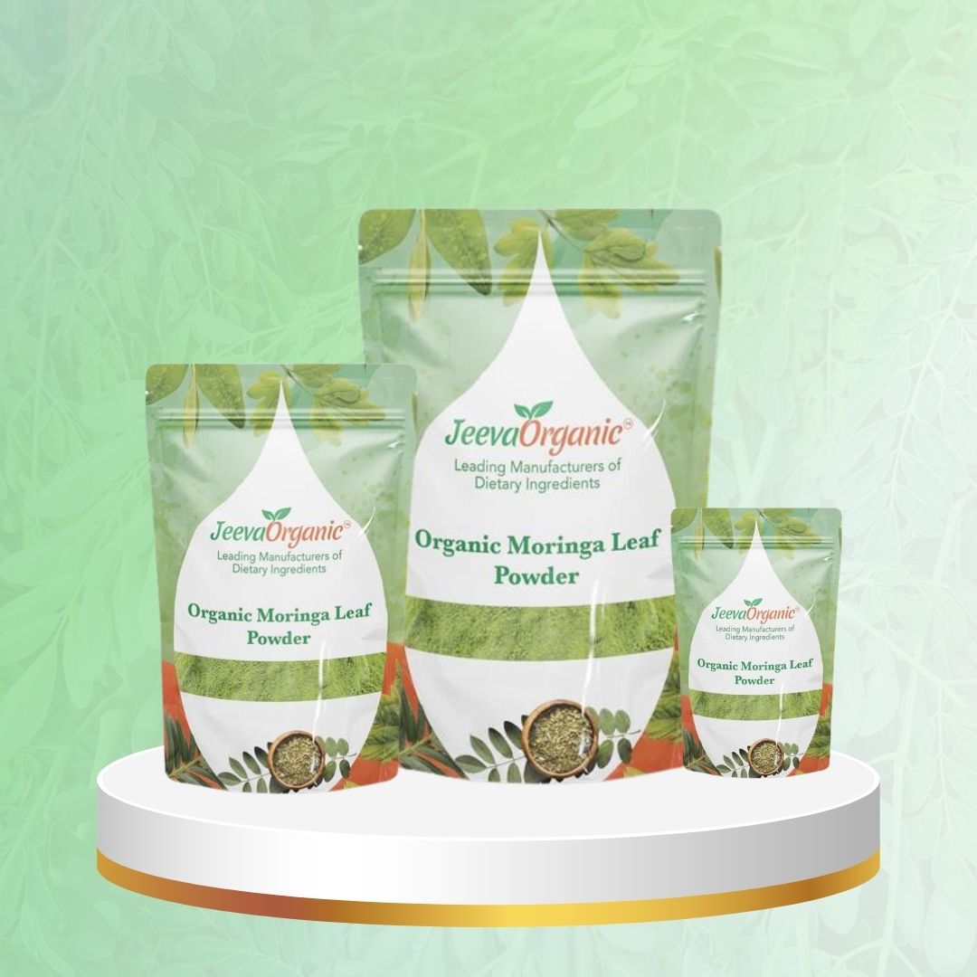 Three packages of Organic Moringa Leaf Powder by Jeeva Organic, displayed on a circular pedestal with a leafy background.